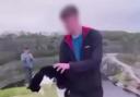 A screenshot from the video where a boy is holding a cat, shortly before throwing it from a cliff