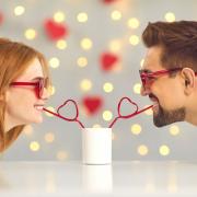 A couple sharing a drink together from two love heart straws. Credit: Canva