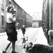 A mum stops to chat to a neighbour mopping the flags outside the front of her home in 1950s Blackburn.