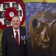 Volunteer arts and crafts co-ordinator at Veterans In Communities Darren Horsnell with the giant rhino oil painting being raffles for charity.